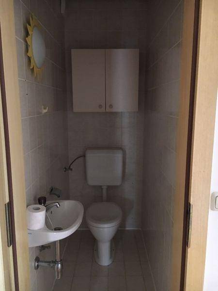 Kleines Gäste-WC mit Fliesenboden, Wand-WC und einem kompakten Waschbecken.