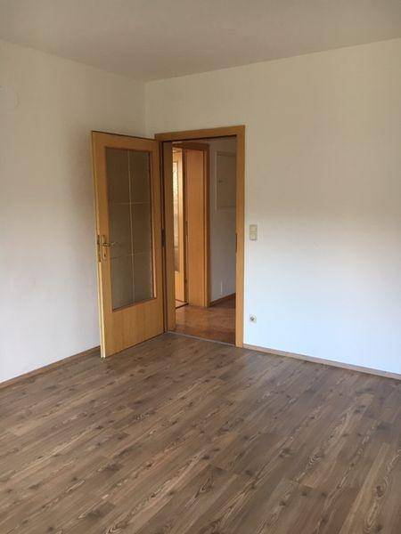 Geräumiges Zimmer mit Laminatboden und einer Tür, die zu einem weiteren Raum führt.