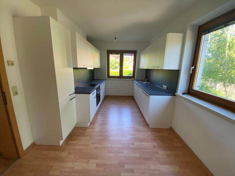 Neue, helle Küche mit weißen Schränken, dunklen Arbeitsplatten und zwei Fenstern.