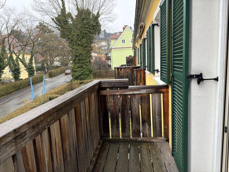 Kleiner Holzbalkon mit Blick auf die Straße und umliegende Bäume.