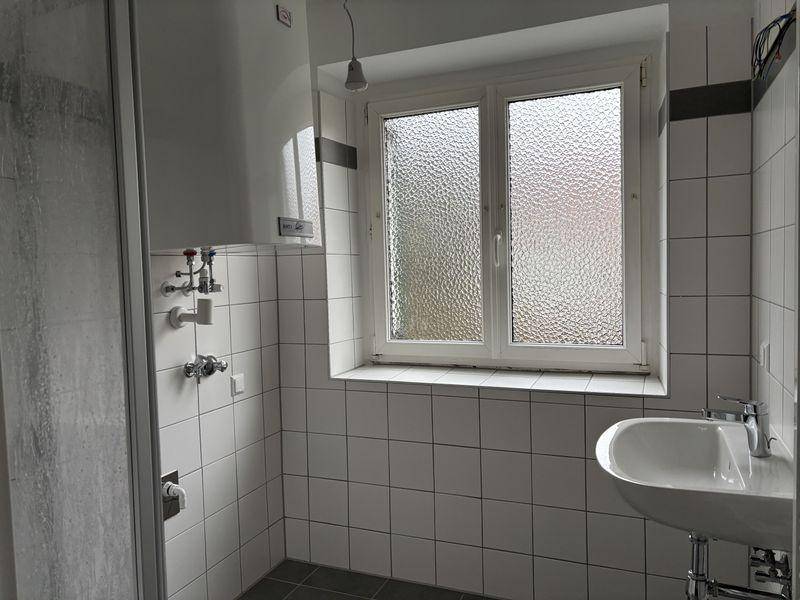 Helles Badezimmer mit weißen Fliesen, Waschbecken und Duschbereich.