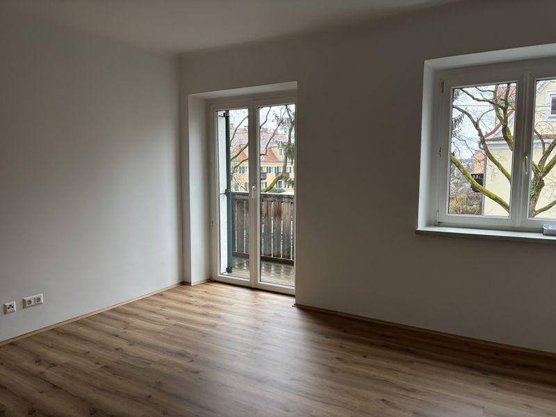 Helles Zimmer mit Laminatboden und Zugang zu einem Balkon.