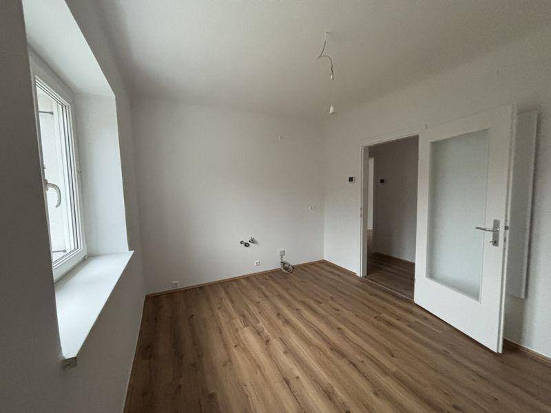Geräumiges Zimmer mit Laminatboden und einer Tür mit Glaseinsatz.