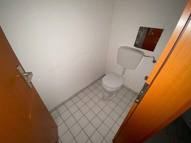 Kleines, einfach gefliestes Gäste-WC mit Toilette und weiß gestrichenen Wänden.