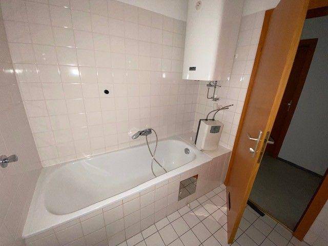 Gefliestes Badezimmer mit Badewanne und Warmwasserboiler, in einem einfachen, funktionalen Zustand.