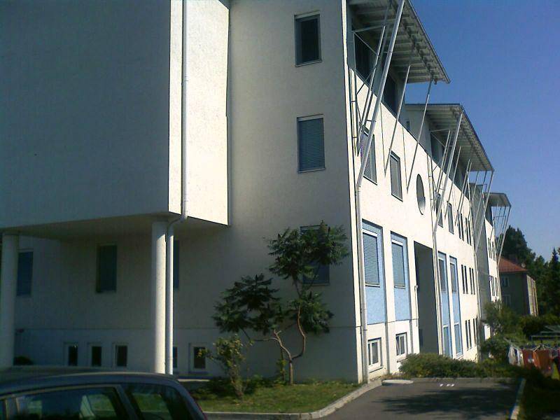 Seitenansicht eines modernen Mehrfamilienhauses mit blauen Akzenten und schattenspendenden Überdachungen.