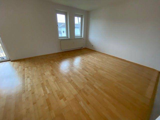 Helles, leeres Wohnzimmer mit glänzendem Parkettboden und zwei Fenstern, bereit zur Einrichtung.