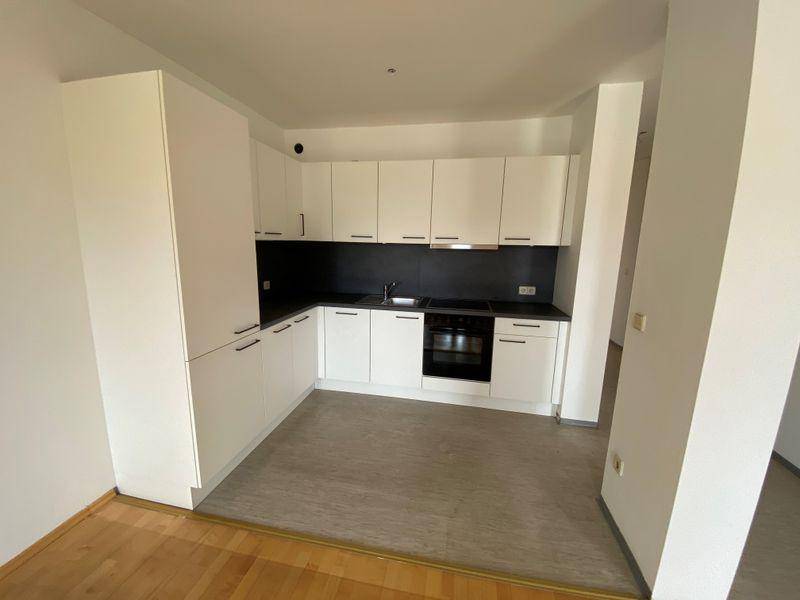 Moderne, neu eingebaute Küche mit weißen Schränken, dunkler Arbeitsplatte und integrierten Geräten.