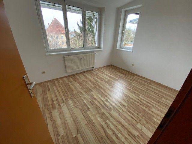 Helles Schlafzimmer mit Laminatboden und großen Fenstern, die viel Tageslicht hereinlassen.