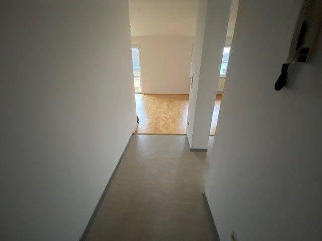Langer Flur mit Vinylboden, der in einen hellen Raum mit Parkettboden übergeht.