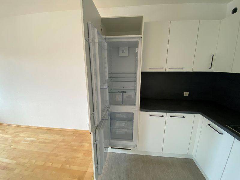 Integrierter Kühlschrank in einer modernen Küche mit weißen Schränken und dunkler Arbeitsplatte.