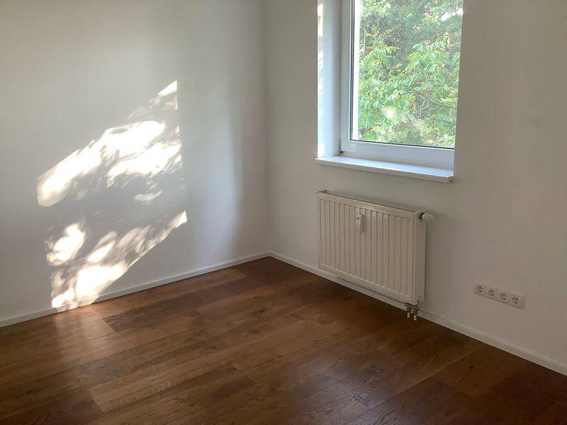 Heller Raum mit Holzboden, Fenster und Heizkörper, bietet einen angenehmen Blick ins Grüne.