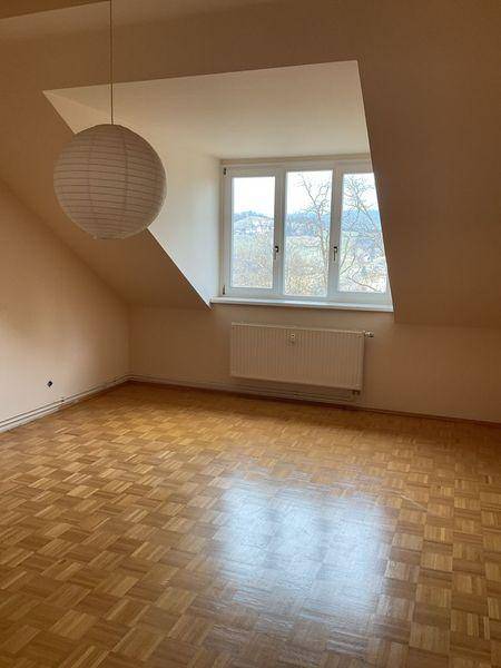 Helles Zimmer im Dachgeschoss mit Parkettboden, schräger Decke und großem Fenster mit Ausblick.
