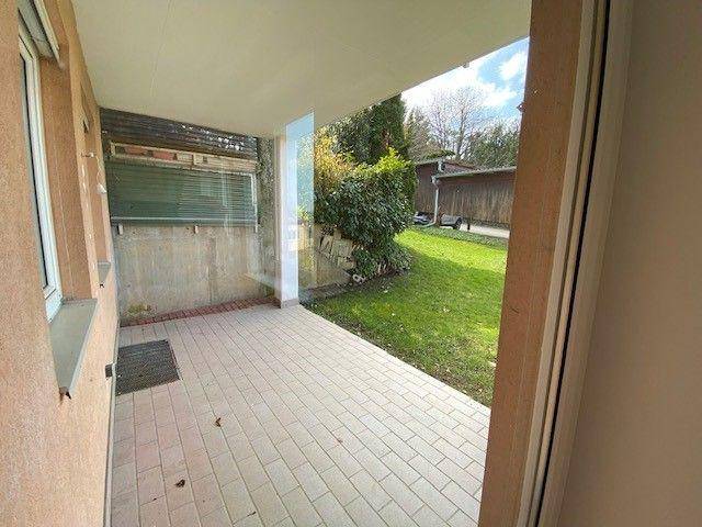Überdachte Terrasse mit hellen Fliesen und Blick auf den kleinen grünen Gartenbereich.