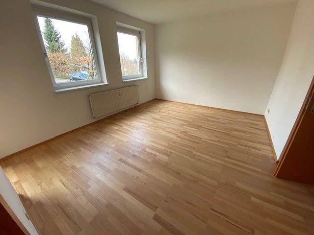 Helles Zimmer mit zwei Fenstern und durchgehendem Laminatboden, ideal als Schlafzimmer.
