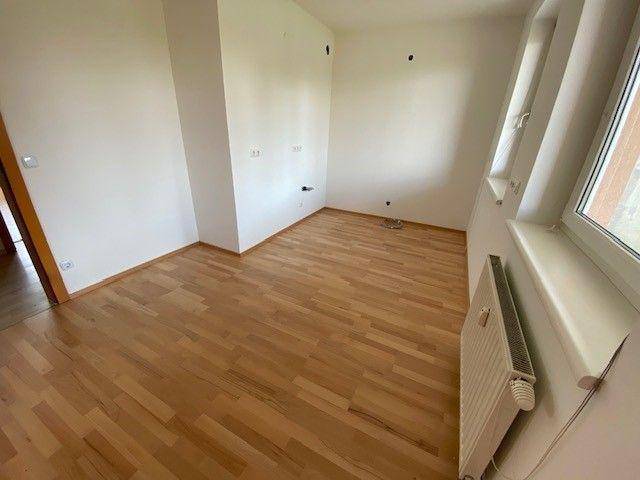 Leerer Küchenraum mit hellem Laminatboden und vorbereiteten Anschlüssen für eine Einbauküche.