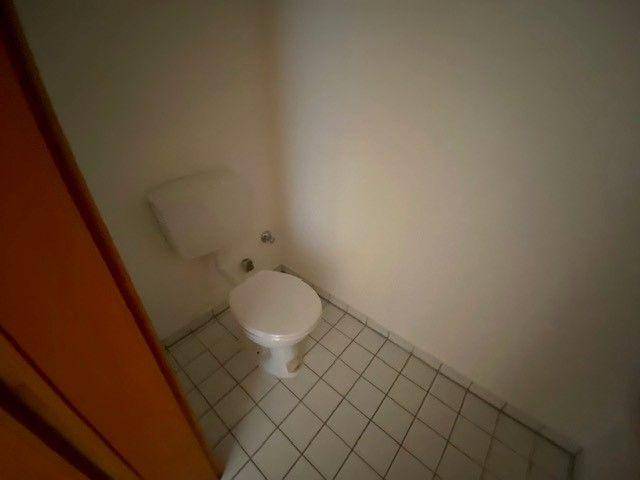 Kleines separates WC mit weißer Toilette und hell gefliestem Boden.