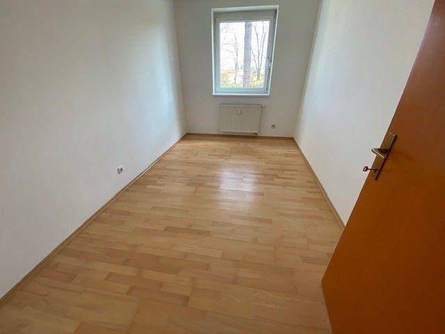 Helles Schlafzimmer mit Laminatboden und einem Fenster, das viel Tageslicht hereinlässt.