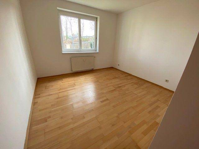 Geräumiges Schlafzimmer mit hellem Laminatboden und einem großen Fenster.