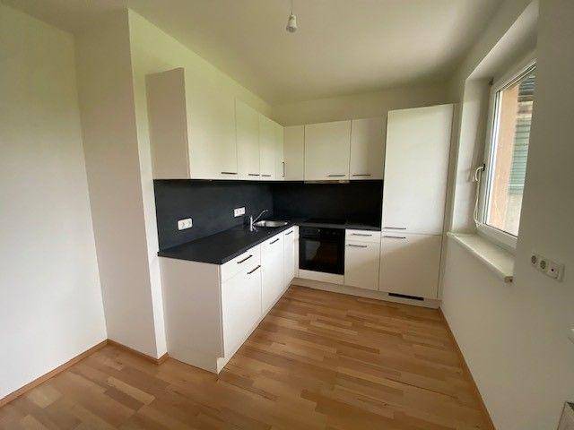 Moderne Einbauküche mit weißen Schränken, dunkler Arbeitsplatte und integrierten Geräten.