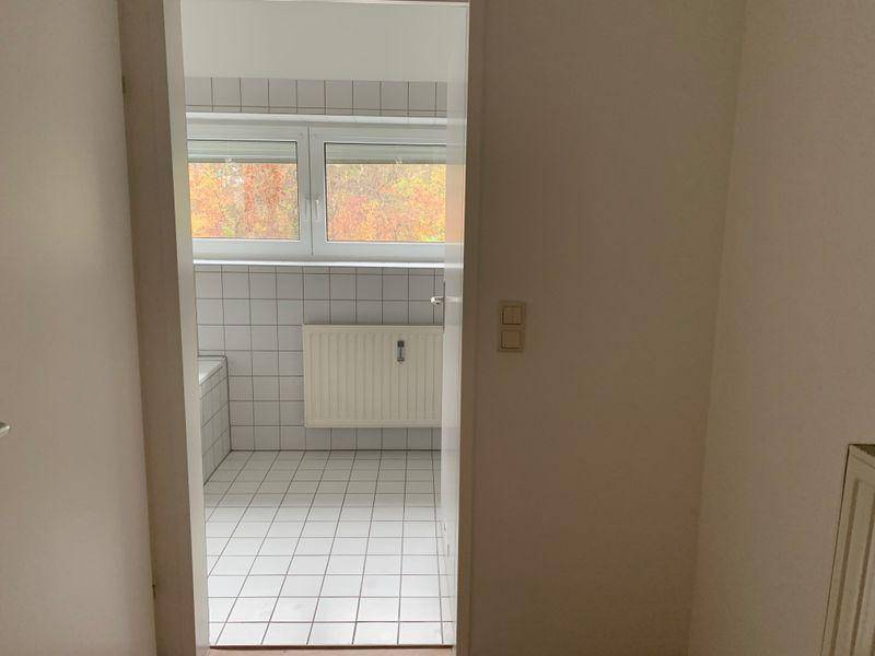 Blick durch eine Tür in ein gefliestes Badezimmer mit Badewanne und Fenster.