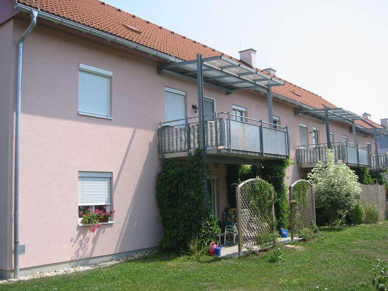 Reihenhausfassade mit mehreren Balkonen, Rankpflanzen und grüner Rasenfläche.