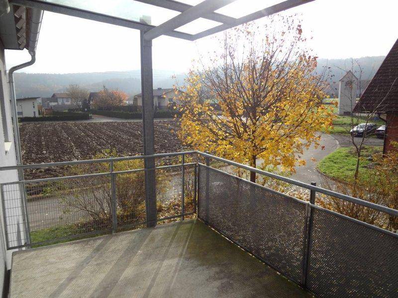 Blick vom Balkon auf ein Feld, Bäume und die umliegende ländliche Bebauung.