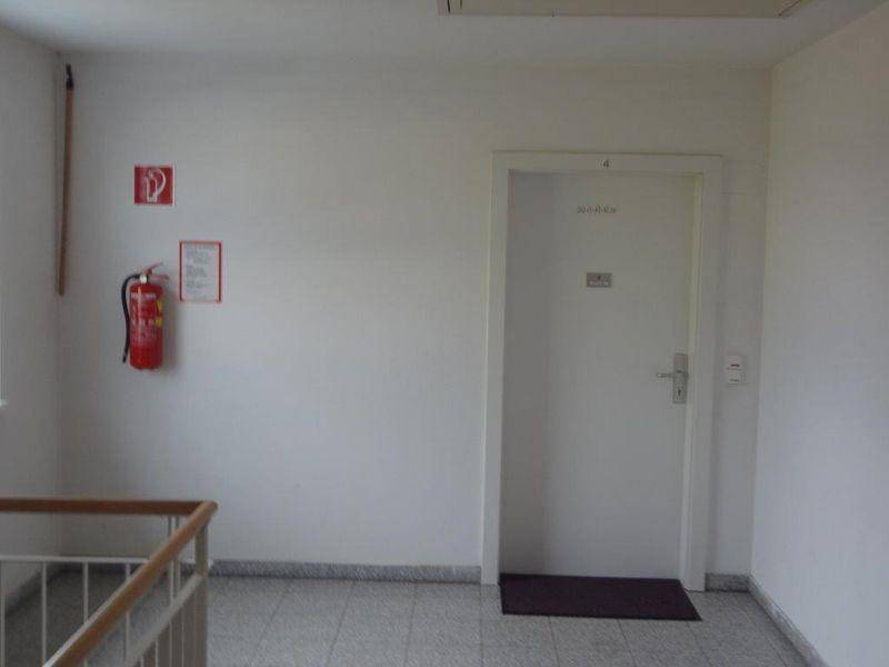 Wohnungstür im Flur mit Feuerlöscher an der Wand und Fliesenboden.