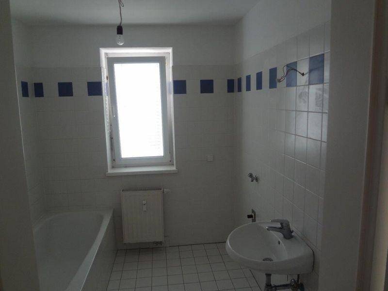 Badezimmer mit Badewanne, Waschbecken, Fenster und weiß-blauen Fliesen.