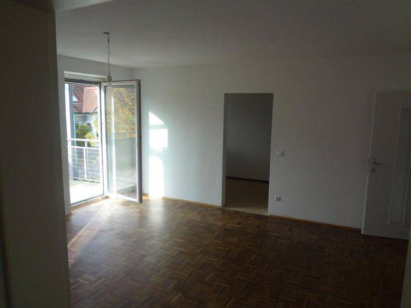 Wohnzimmer mit Parkettboden und Zugang zu einem sonnigen Balkon.