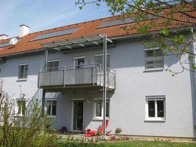 Gebäudeansicht mit Balkon, Solarpaneelen auf dem Dach und gepflegtem Gartenbereich.