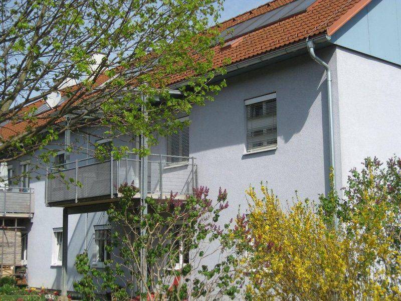Seitenansicht des Gebäudes mit Balkonen, Bäumen und blühenden Sträuchern.