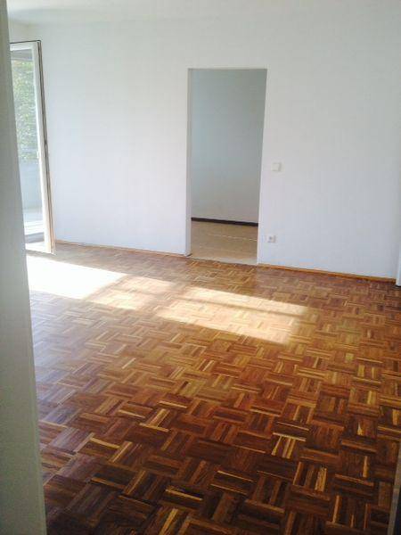 Helles Zimmer mit Parkettboden und Sonneneinstrahlung durch die Türöffnung.