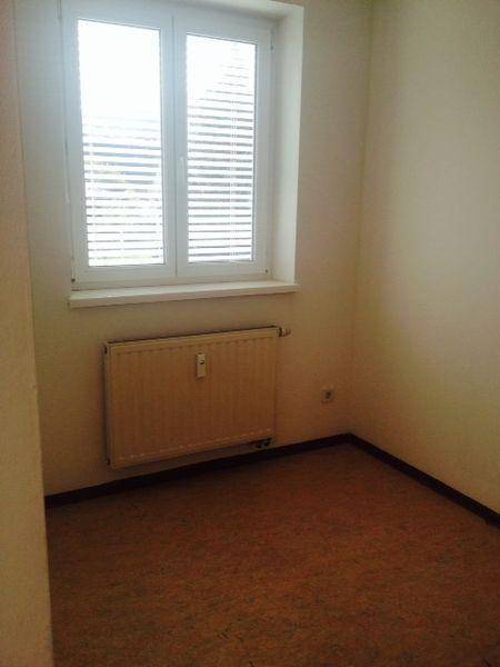 Leeres Zimmer mit Laminatboden, Fenster mit Jalousien und Heizkörper.
