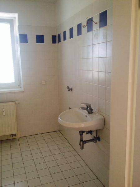 Badezimmer mit Waschbecken, Fenster und weiß-blauen Fliesen an der Wand.