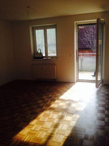 Helles Zimmer mit Parkettboden, Fenster mit Jalousien und Heizkörper.