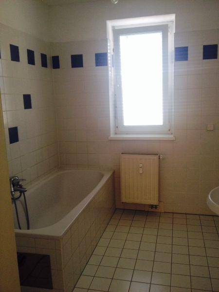 Badezimmer mit Badewanne, Fenster und weiß-blauen Wandfliesen.