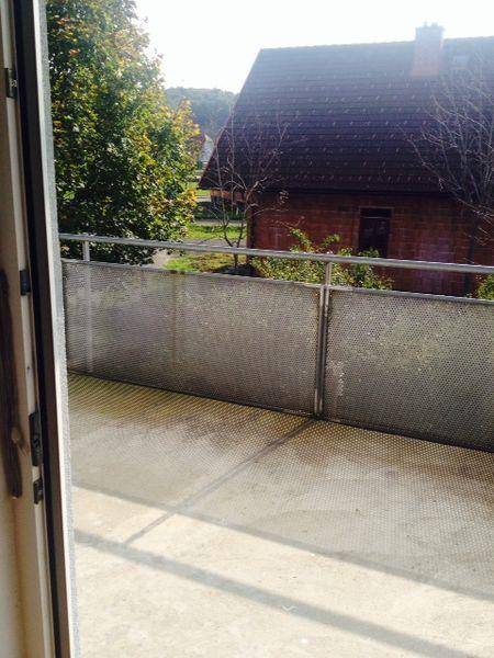 Blick vom Balkon auf ein Nachbarhaus mit Ziegeldach und Bäume.