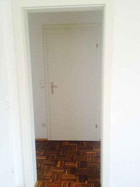 Heller Flur mit Holzboden und weißer Tür, die zu einem weiteren Raum führt.