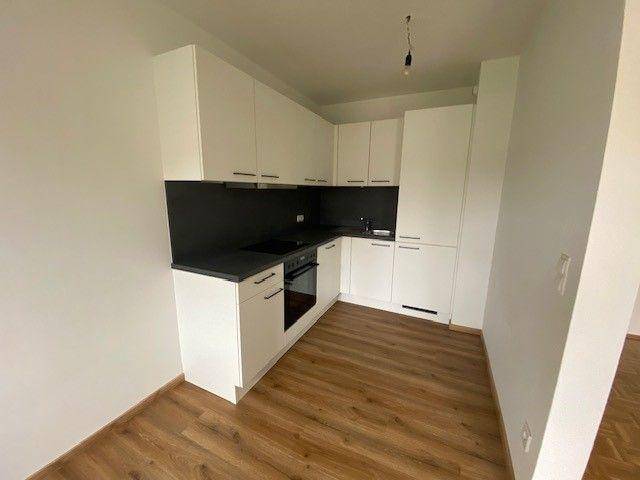 Moderne Einbauküche mit weißen Schränken, dunkler Arbeitsplatte und Laminatboden.