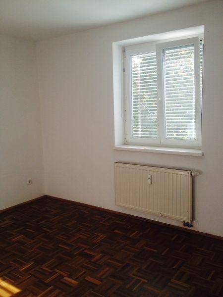 Leeres Zimmer mit Parkettboden und einem Fenster mit Jalousien.