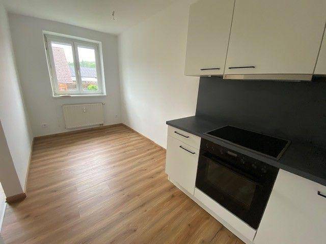 Helle Küche mit Fenster, weißen Schränken und Laminatboden.
