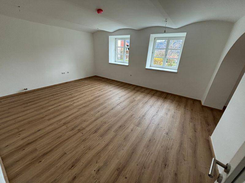 Geräumiger Wohnbereich mit modernem Laminatboden und zwei Fenstern mit Bergblick.