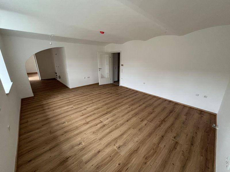Heller Wohnraum mit Laminatboden, weißen Wänden und Zugang zu weiteren Zimmern.