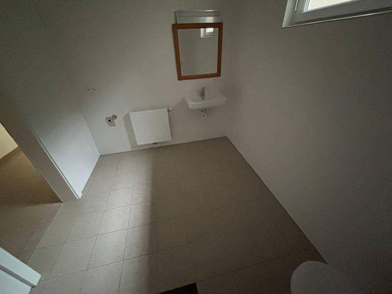 Helles WC mit Waschbecken, Spiegel und Heizkörper, ausgestattet mit beigefarbenen Fliesen.