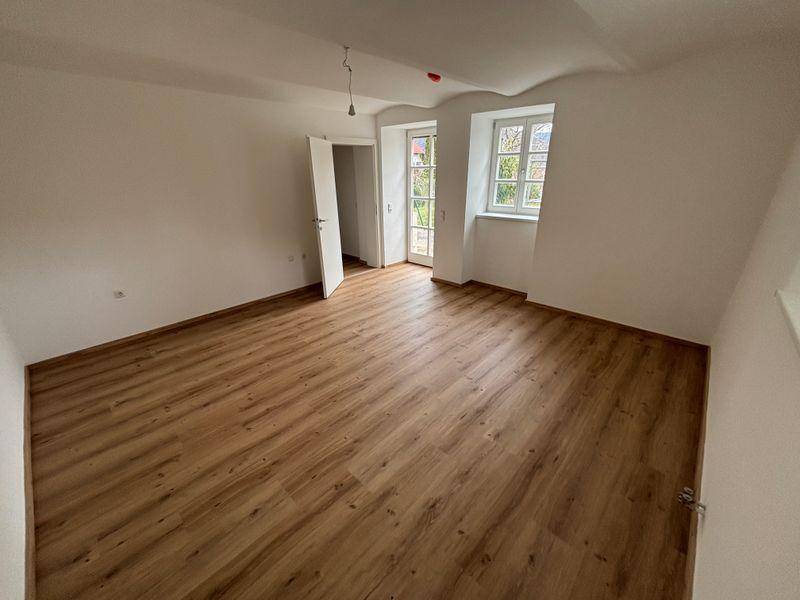 Heller Raum mit Laminatboden, weiß gestrichenen Wänden und Zugang zu einem Balkon oder Terrasse.