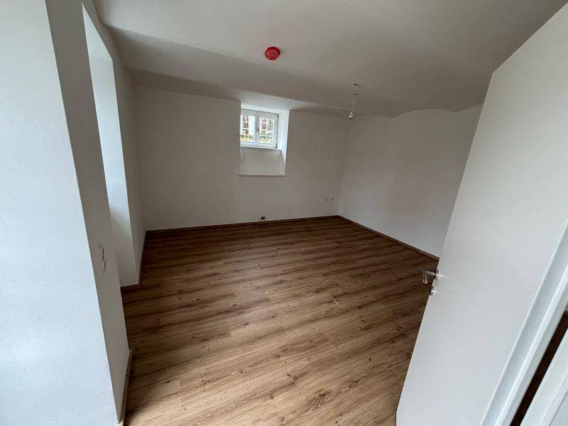 Gemütliches Schlafzimmer mit Laminatboden, weiß gestrichenen Wänden und einem Fenster.