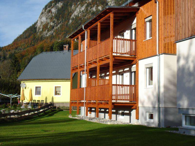 Ansicht eines modernen Hauses mit Holzbalkonen und gepflegtem Rasen vor einer Bergkulisse.