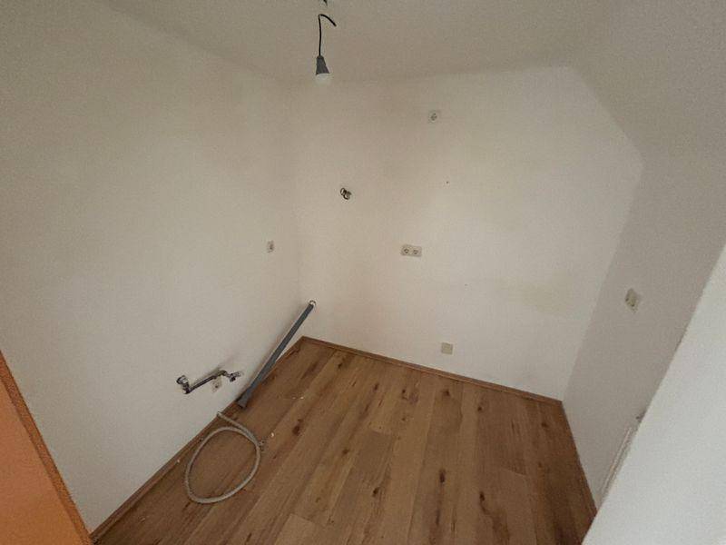 Leerer Raum mit Holzboden und sichtbaren Anschlüssen für eine zukünftige Küche oder Hauswirtschaftsraum.