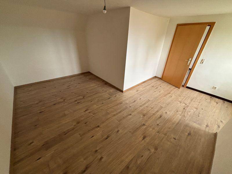 Leeres Zimmer mit hellem Holzboden und einer Holztür, bereit zur individuellen Gestaltung.